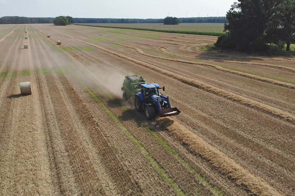 New Holland Traktor mit John Deere V461R Rundballenpresse bei der Strohernte