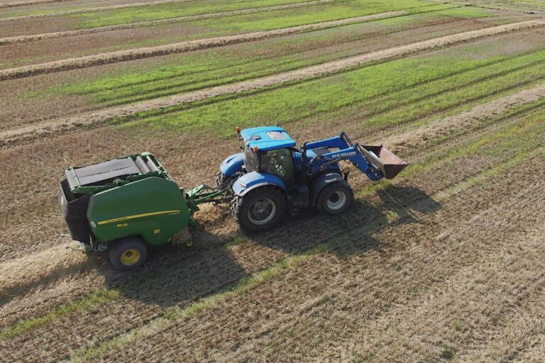 New Holland Traktor mit John Deere V461R Rundballenpresse bei der Arbeit